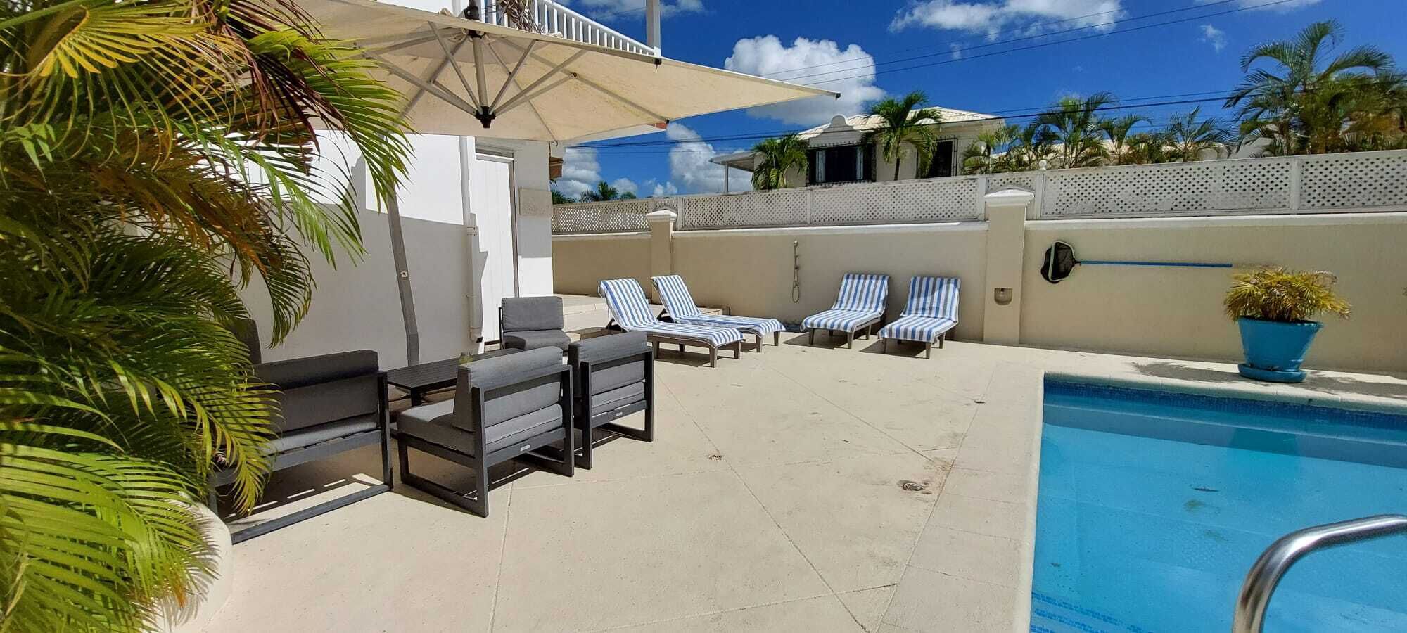 A poolside area with lounge chairs, a small table, and a pool.