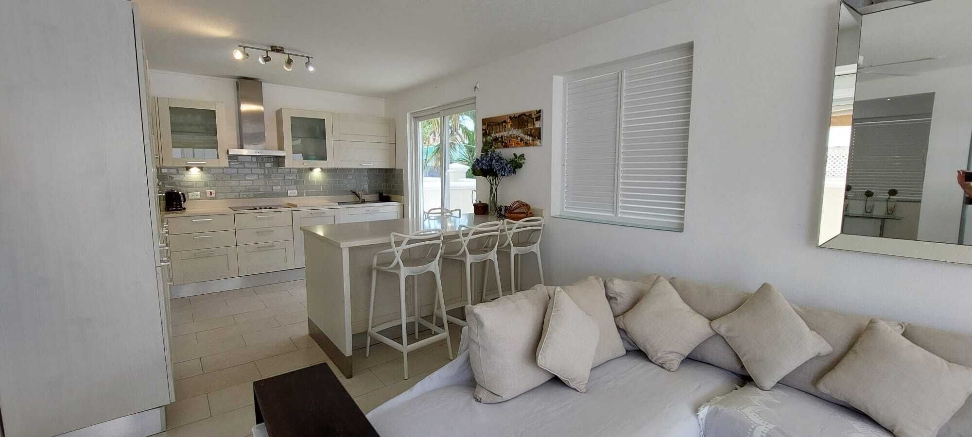 A modern kitchen with white cabinets, a central island with bar stools, and a dining area.
