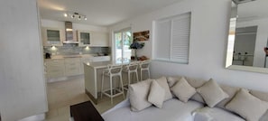 A modern kitchen with white cabinets, a central island with bar stools, and a dining area. - Airy 3BR Home with Shared Pool, Close to Beach (Porters, Saint James)