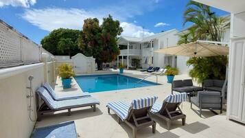 A pool area with lounge chairs, a covered seating area, and a house in the background.