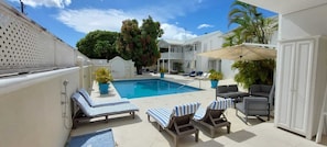 A pool area with lounge chairs, a covered seating area, and a house in the background. - 3BR Caribbean Home in Porters | Walk to Beach & Pool (Porters, Saint James)