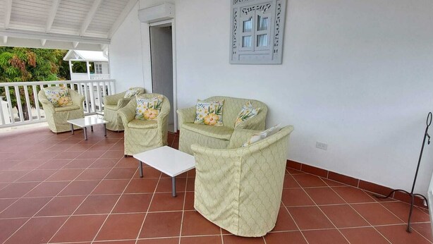 Eine überdachte Terrasse mit zwei gepolsterten Stühlen und einem kleinen Tisch, weißen Geländern und einem gefliesten Boden.