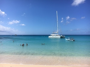 A beach with a sailboat anchored near the shore, clear turquoise water, and a few people swimming. - 3BR Caribbean Home in Porters | Walk to Beach & Pool (Porters, Saint James)