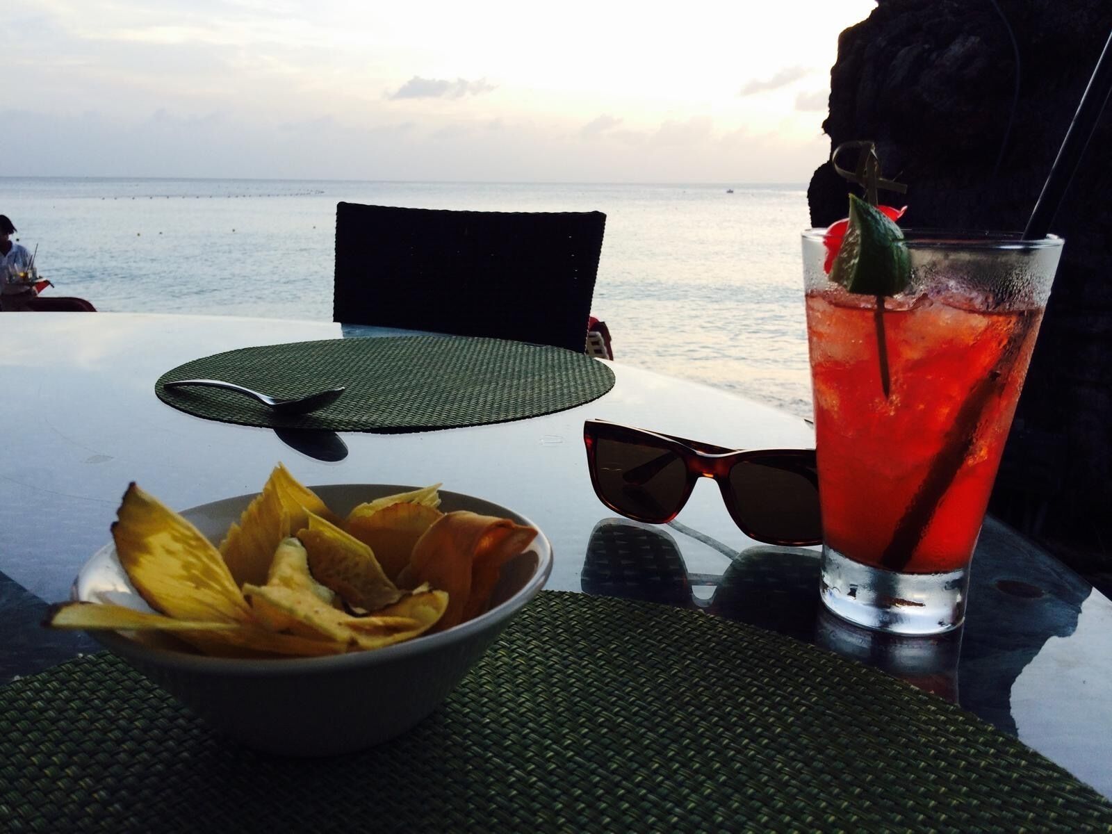 A table with a glass of red beverage, a bowl of chips, and a pair of sunglasses.