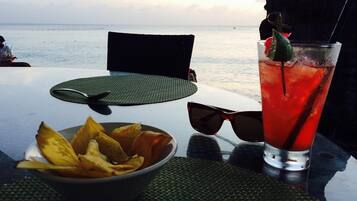 A table with a glass of red beverage, a bowl of chips, and a pair of sunglasses.