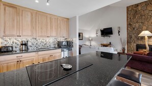 Een moderne keuken met houten kastjes, een groot eiland met een zwart aanrecht en een stenen muur op de achtergrond.