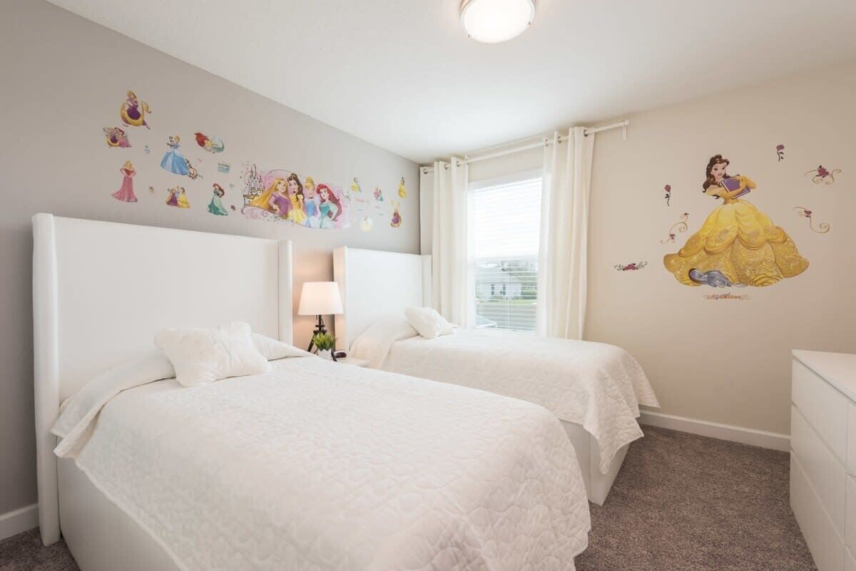 A bedroom with two beds, a window with curtains, and a wall with Disney princess stickers.