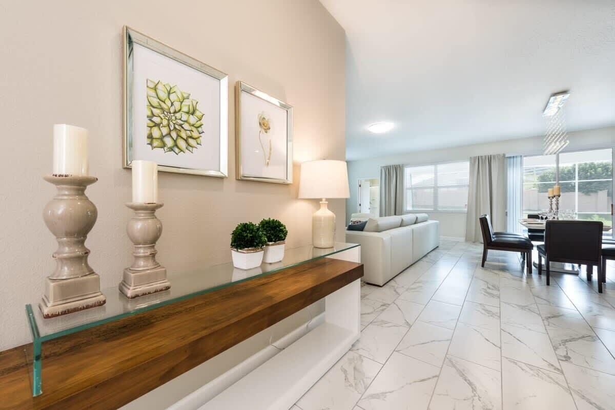 A modern living room with a glass coffee table, a sofa, a dining area with a table and chairs, and framed artwork on the wall.