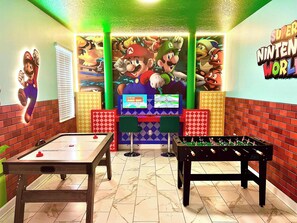 Huoneessa on pöytäjalkapallopeli, biljardipöytä ja seinämaalaus, jonka teemana on Nintendo.