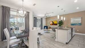 A modern kitchen with a central island, a dining area with white chairs, and a living space with a sofa and TV. - Magical Retreat, Spacious Villa 10 min From Disney (Kissimmee)