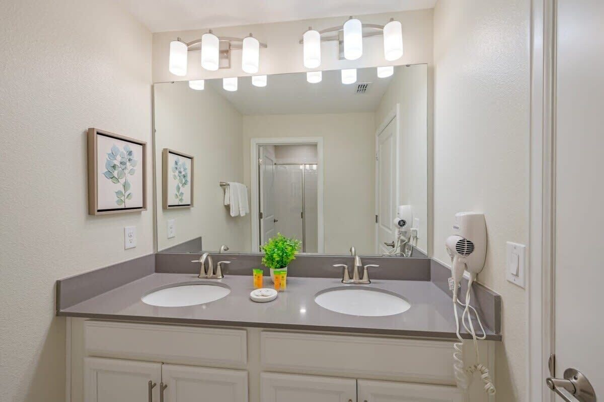 A bathroom with two sinks, a large mirror, and a hairdryer on the wall.