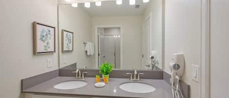 A bathroom with two sinks, a large mirror, and a hairdryer on the wall.