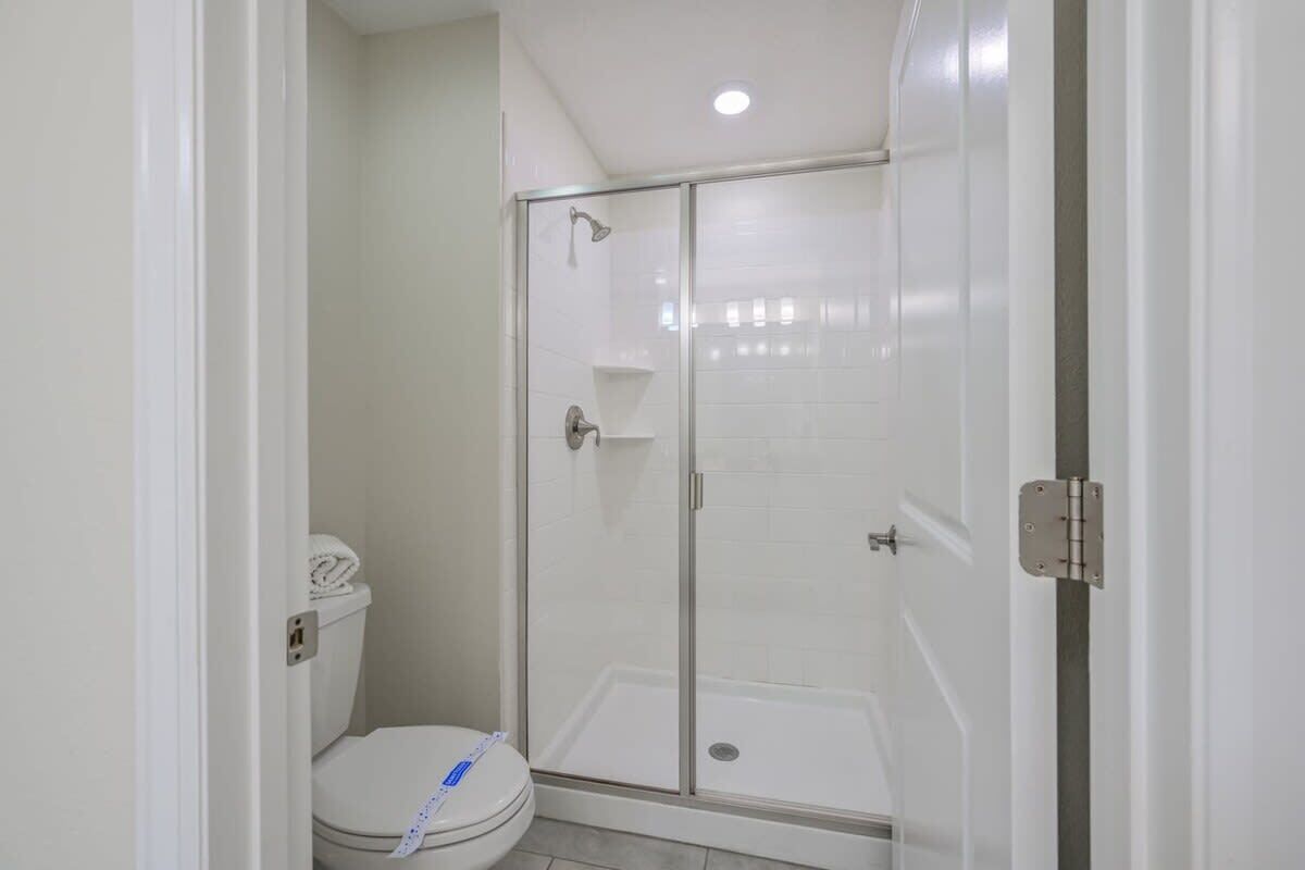 A bathroom with a toilet, a glass-enclosed shower, and a white tiled wall.
