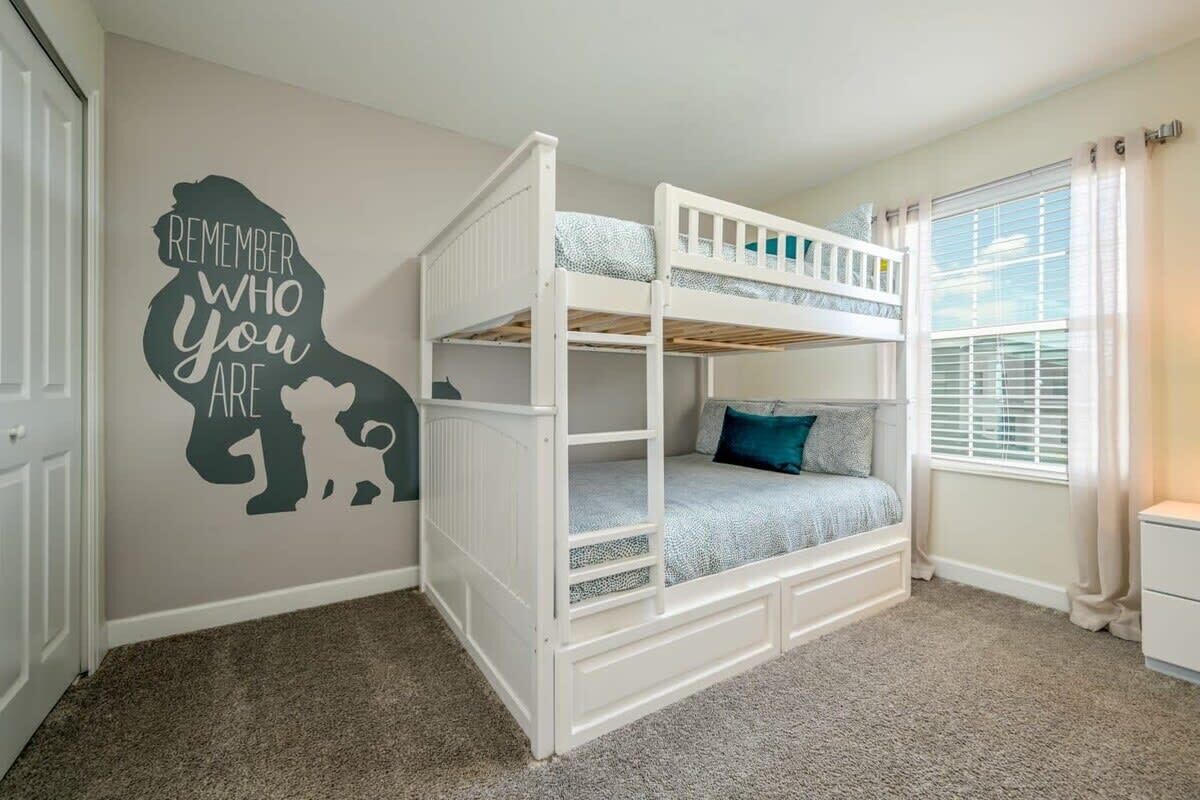 A bunk bed room with a motivational wall decal, a window with blinds, and a carpeted floor.