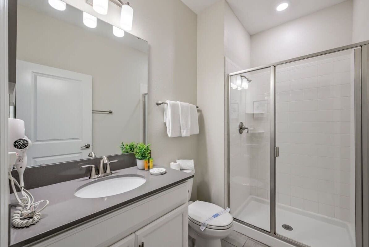 A modern bathroom with a large mirror, a sink, a toilet, and a glass-enclosed shower.