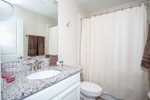 A bathroom with a white sink, a mirror, a toilet, and a shower curtain. - Home 6BR - Prime Location (Kissimmee)