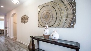 A hallway with a glass-top console table, decorative vases, and a large wall art piece. - Home 6BR - Prime Location (Kissimmee)