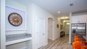 A modern kitchen with a stainless steel refrigerator, a clock on the wall, and a seating area with orange chairs. - Home 6BR - Prime Location (Kissimmee)