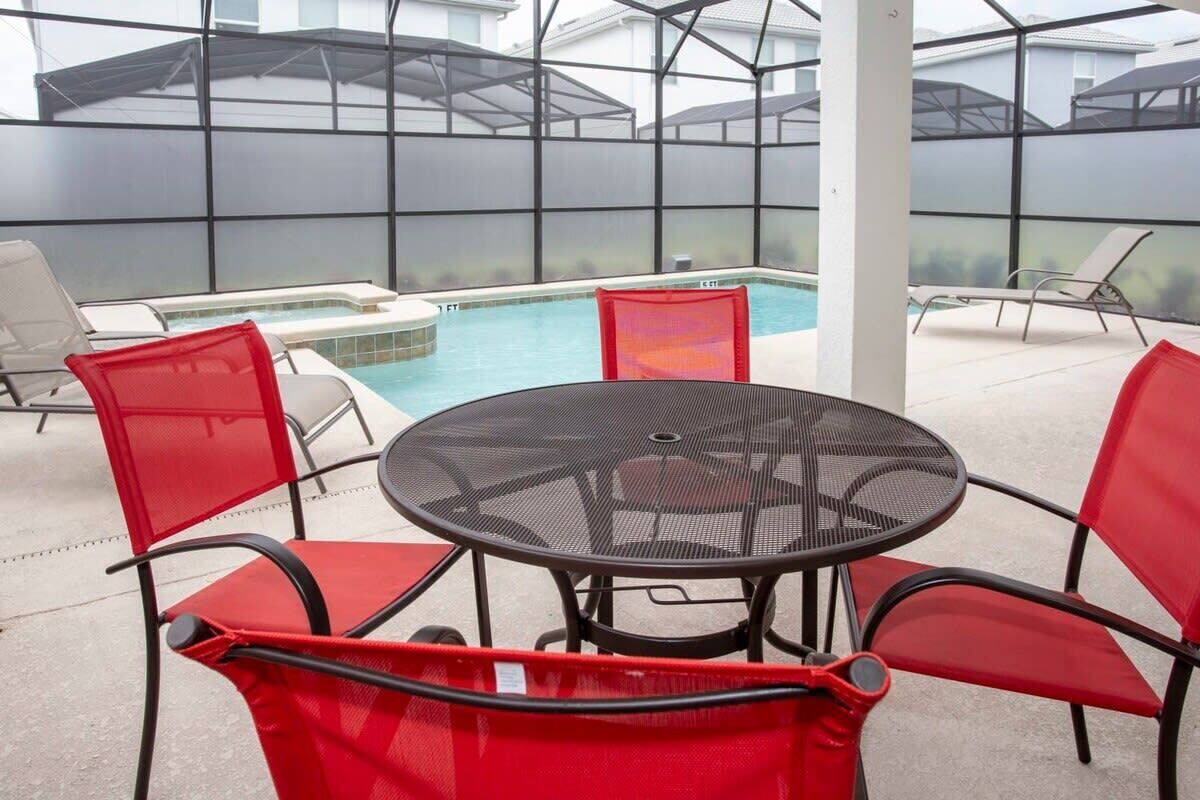 A covered outdoor area with a pool, red chairs, and a round table.