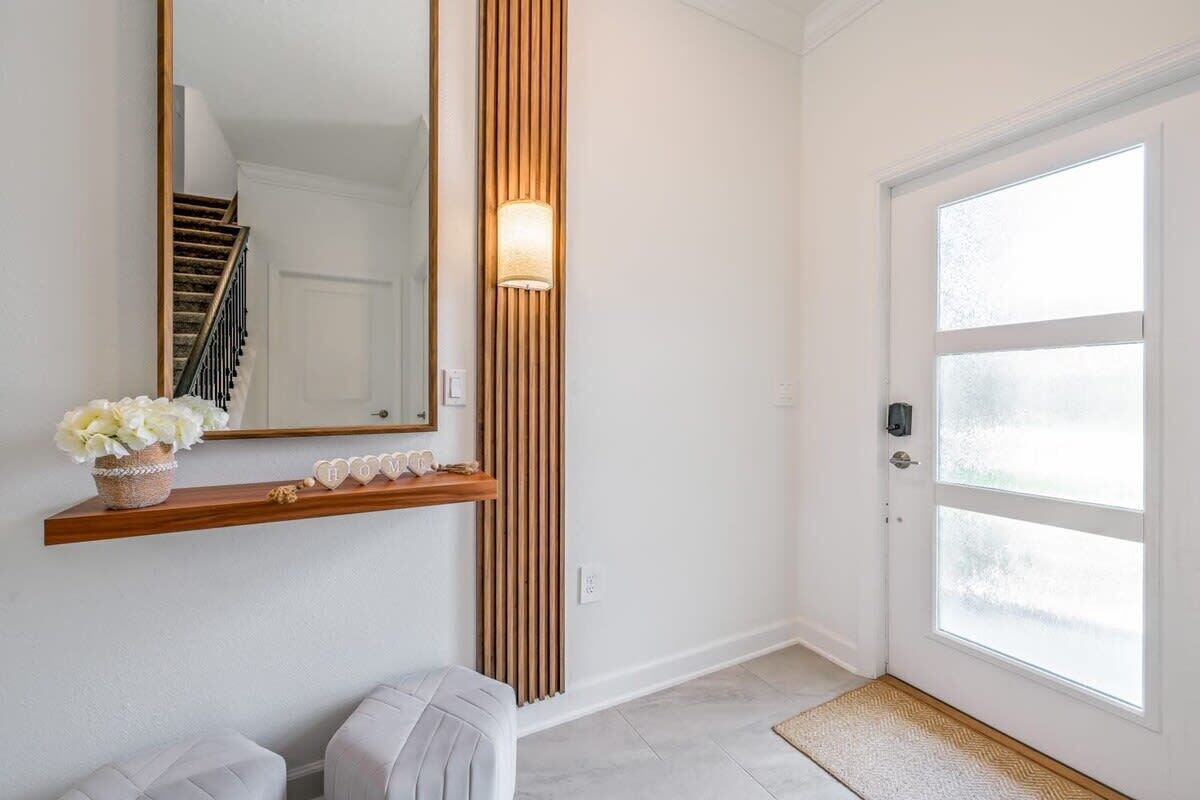 A hallway with a white door, a wooden bench, a mirror, and a shelf with decorative items.