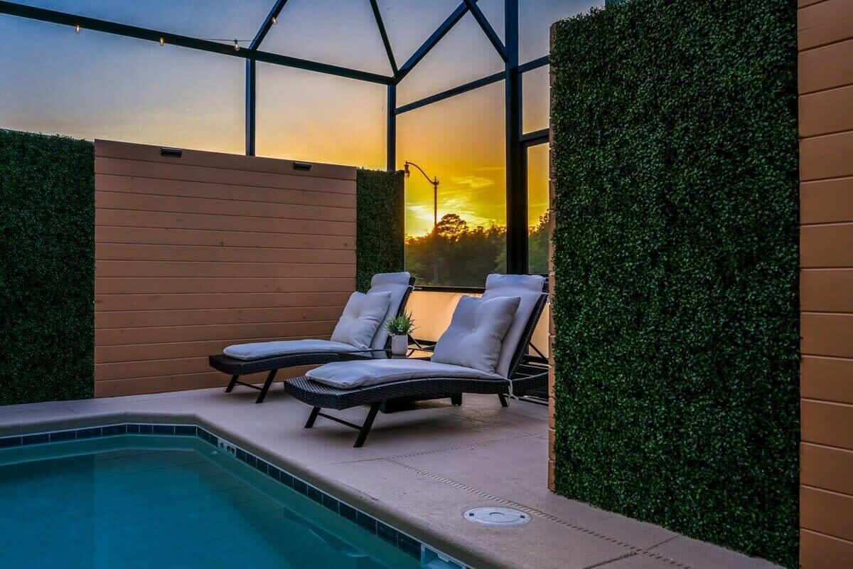 A pool area with lounge chairs and a view of the sunset through a greenhouse structure.