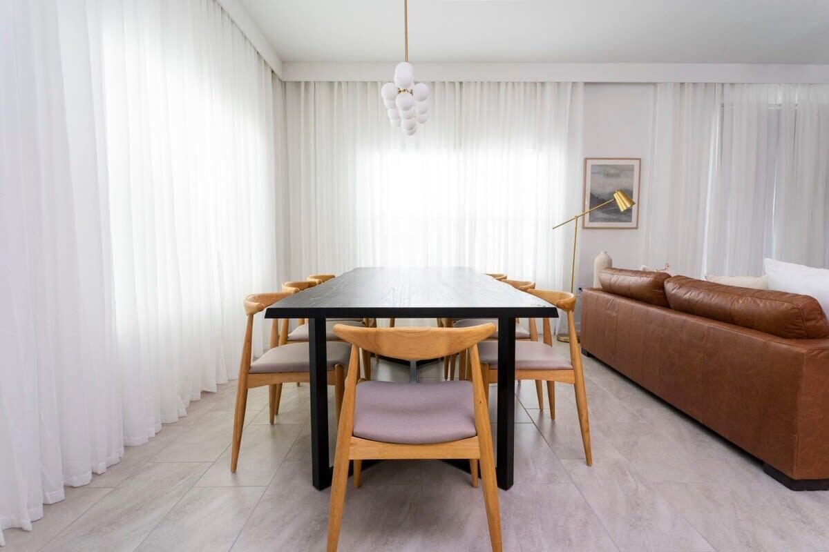 Ett modernt matområde med ett svart bord och trästolar, en brun lädersoffa och en hängande lampa.