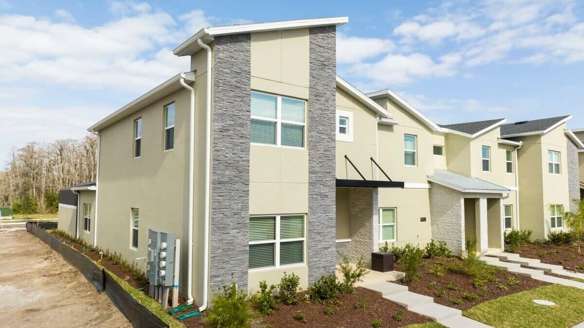 A modern multi-story residential building with a flat roof, large windows, and a landscaped front yard.