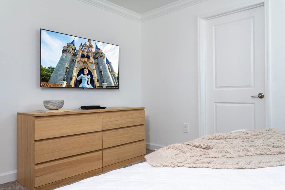 A bedroom with a bed, a wooden dresser, a television displaying a castle, and a white door.
