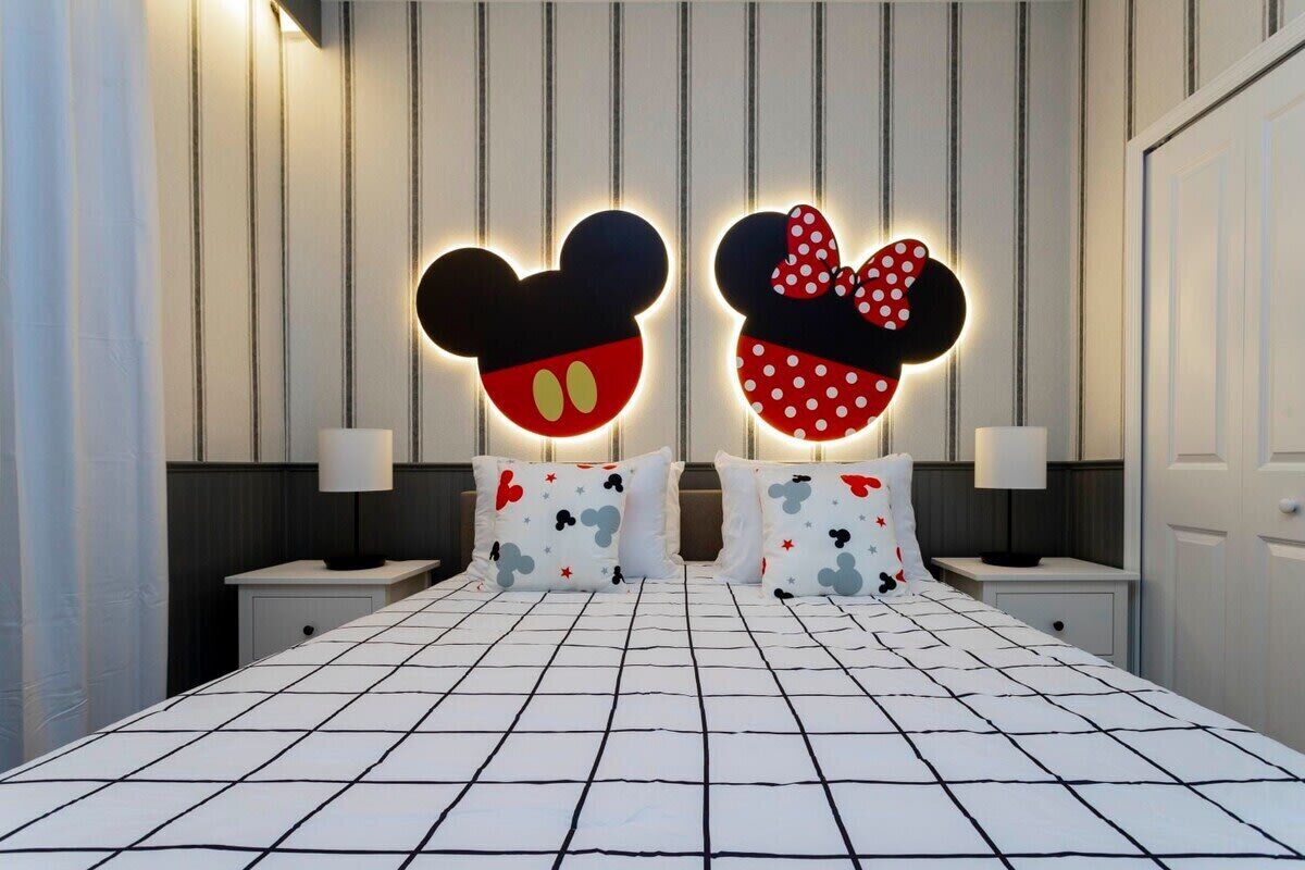 A bed with Mickey Mouse and Minnie Mouse head-shaped light fixtures, a striped wall, and a white bedspread.