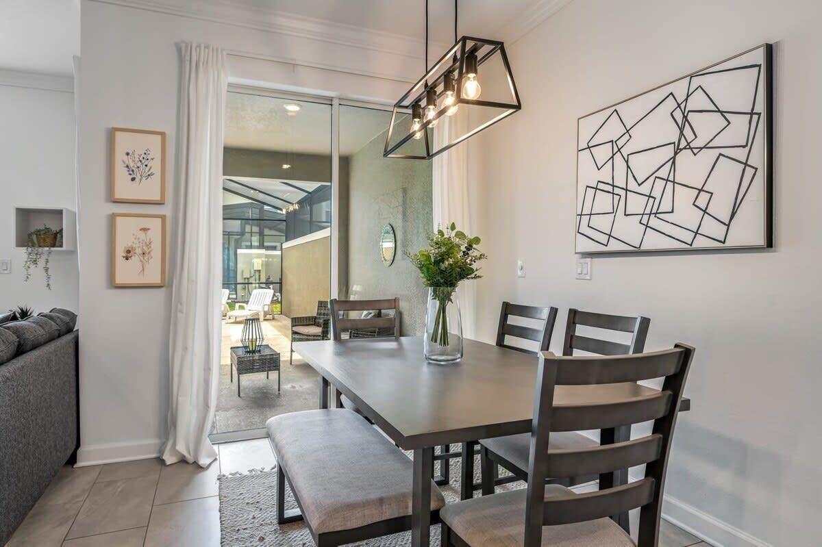 A modern dining area with a wooden table, dark chairs, and a vase with greenery.