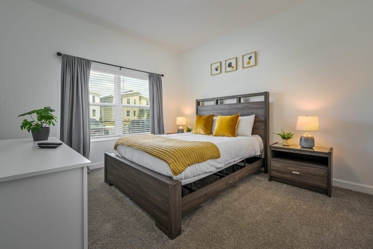 A bedroom with a bed, bedside tables, a desk, and a window with curtains.