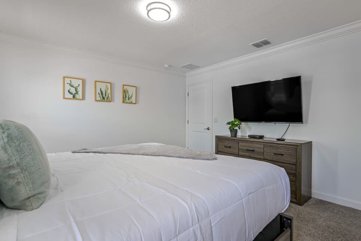 A bedroom with a bed, a dresser, a television, and wall art.