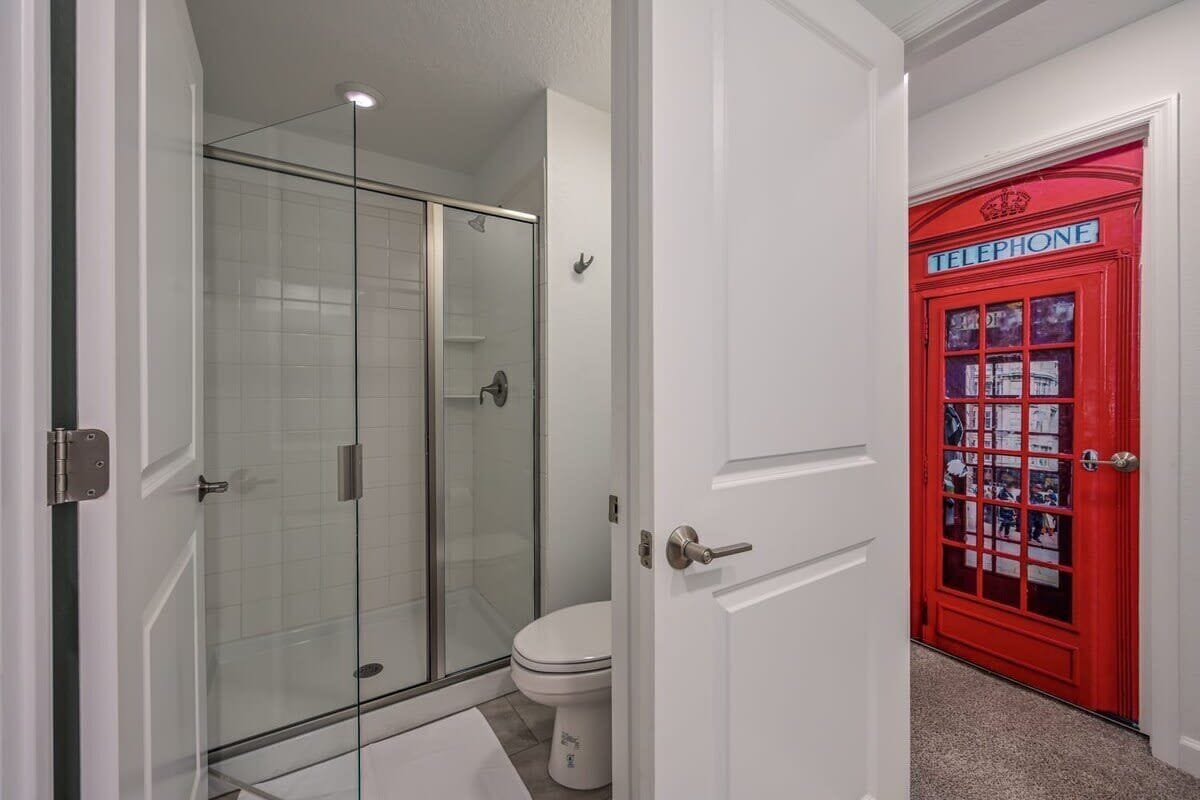 Een badkamer met een douchecabine van glas, een toilet en een rode telefooncel.