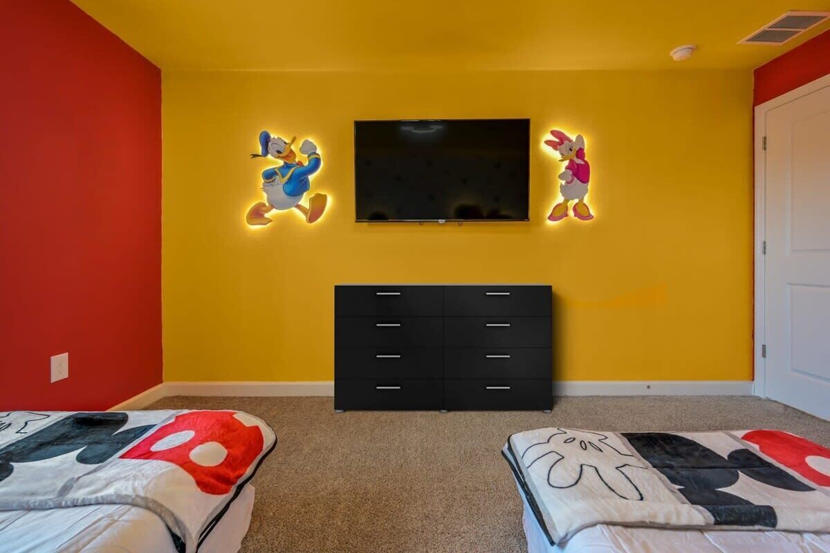 A bedroom with two beds, a TV on the wall, and a dresser.