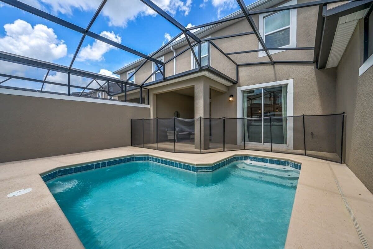 A swimming pool with a glass enclosure, a covered patio area, and a view of the sky.