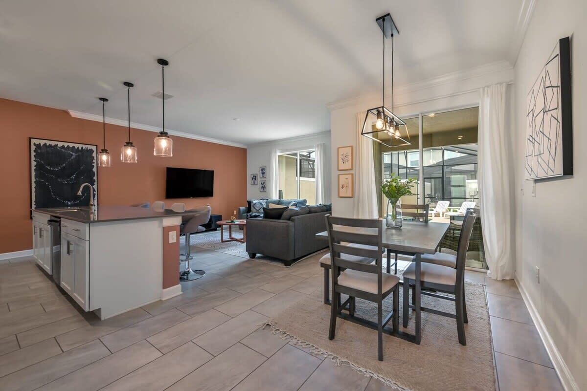 Une cuisine moderne dotée d’un îlot central, un coin repas avec une table et des chaises, et un salon avec un canapé et un téléviseur.