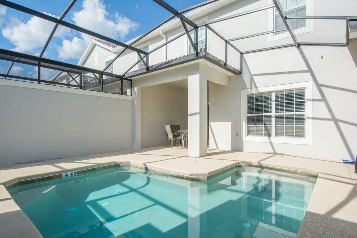Una piscina con techo de vidrio, un área de patio con mesa y sillas, y vista a un edificio al fondo.