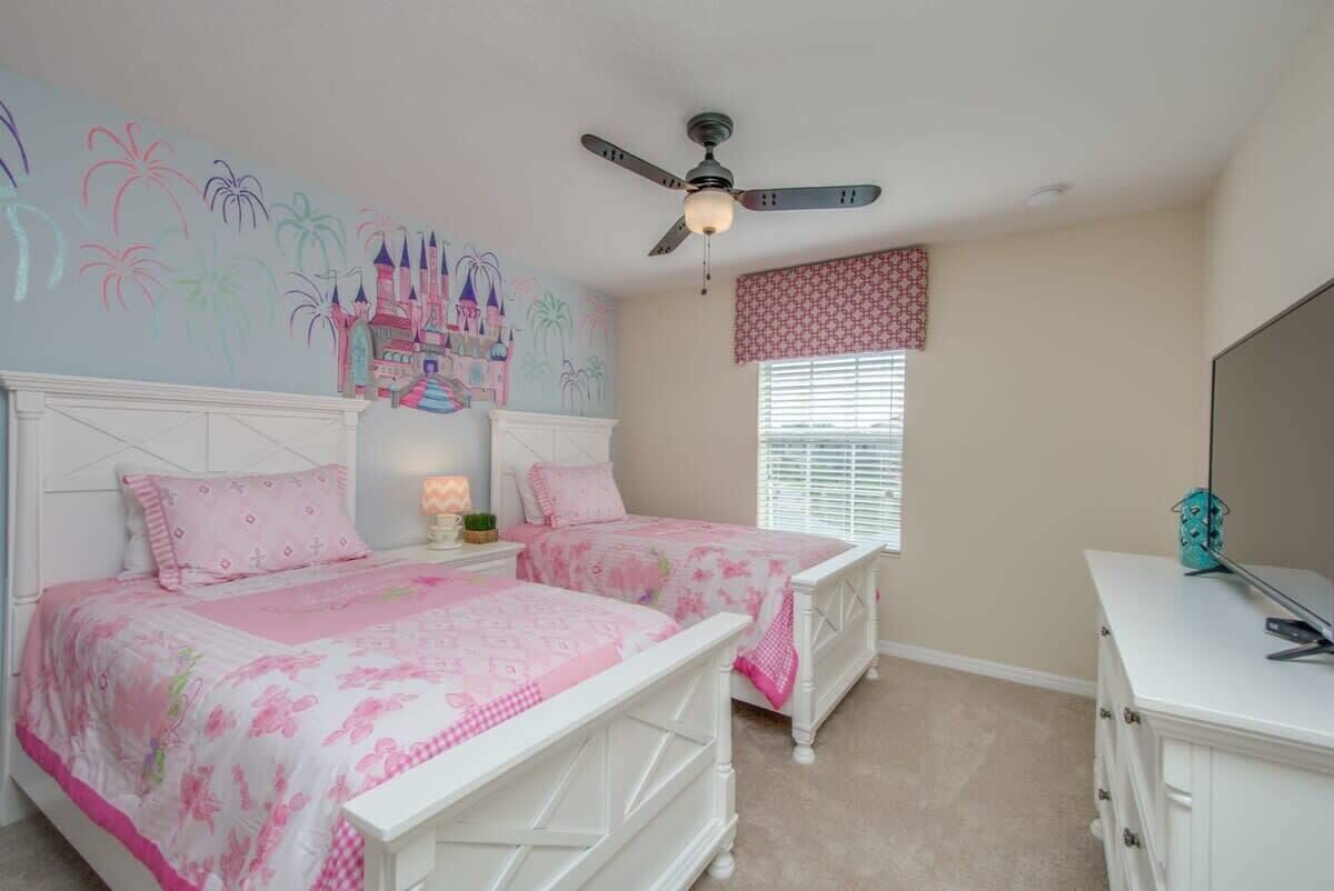 A bedroom with two beds, a ceiling fan, a window with blinds, and a wall mural.