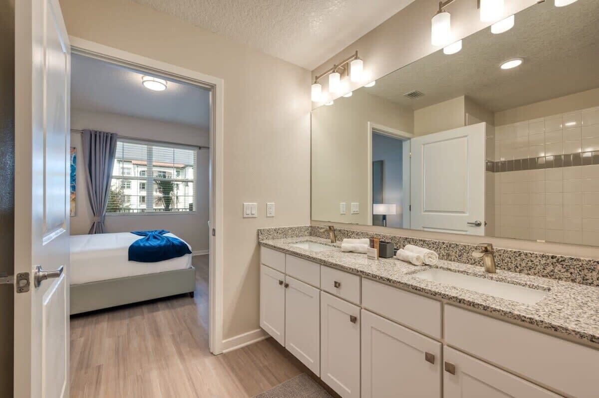 A modern bathroom with a large mirror, two sinks, and a window with curtains.