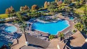 Un resort con una gran piscina central, varias piscinas más pequeñas y un paisaje bien cuidado con palmeras y vistas al agua.