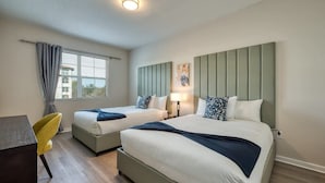 Habitación de hotel con dos camas, un escritorio, una silla, un ventanal con cortinas y una lámpara fijada a la pared.