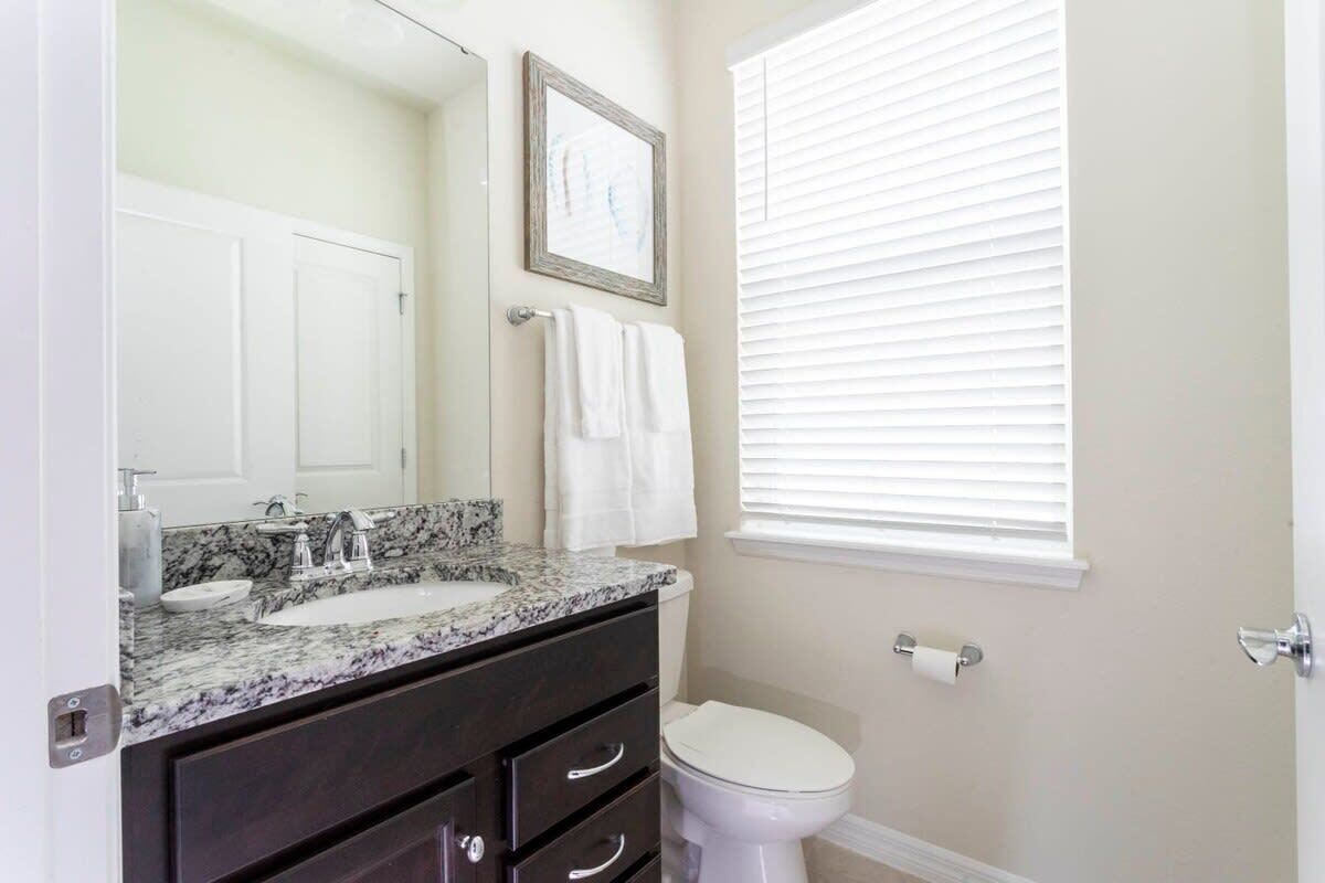 Une salle de bain avec un lavabo en marbre, un meuble-lavabo foncé, des toilettes blanches et une fenêtre avec des stores.