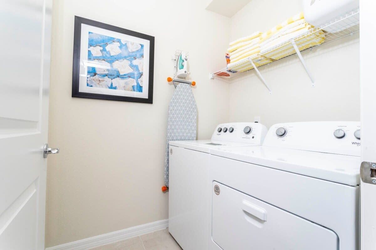A laundry room with a washing machine, an ironing board, and a shelf with laundry supplies.