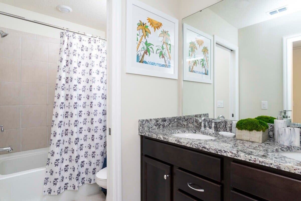Un baño con cortina de ducha, un lavabo con encimera de mármol y un espejo.