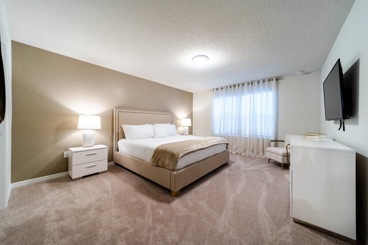 A hotel room with a bed, bedside tables, a TV, and a desk.
