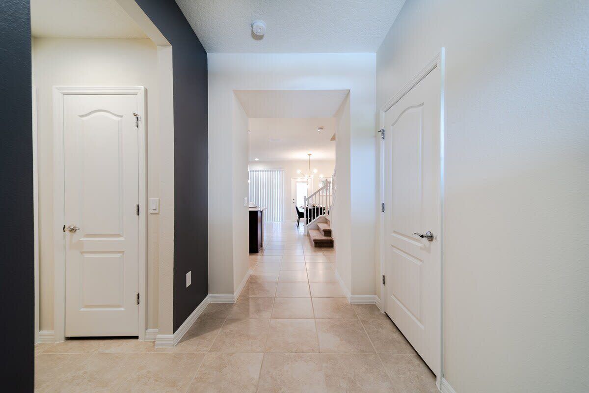 A hallway with white doors, a staircase, and a dining area in the background.
