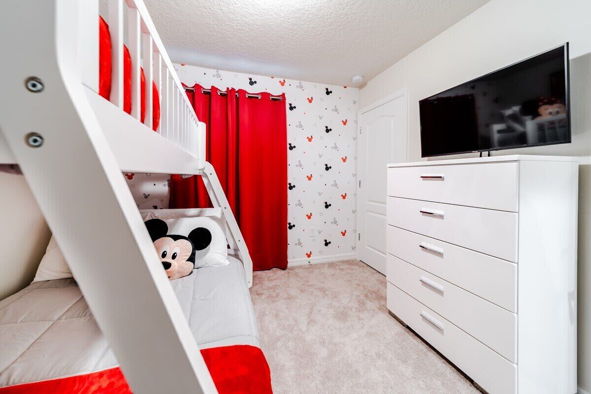 Et børneværelse med køjeseng, fjernsyn, kommode og Mickey Mouse-tema.