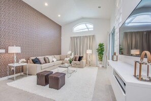 A modern living room with a sectional sofa, a coffee table, a white rug, a large window, and a decorative plant. - Premium Comfort - Beautiful Home, Private Pool (Kissimmee)