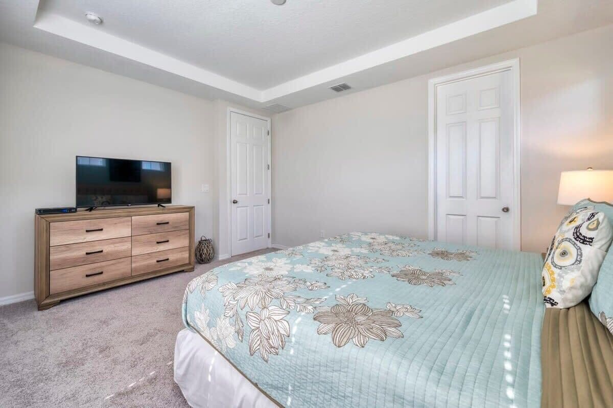 Une chambre à coucher comprenant un lit, une commode, un téléviseur et deux portes.