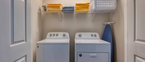 A laundry room with two washing machines, a drying rack, and shelves with folded towels.